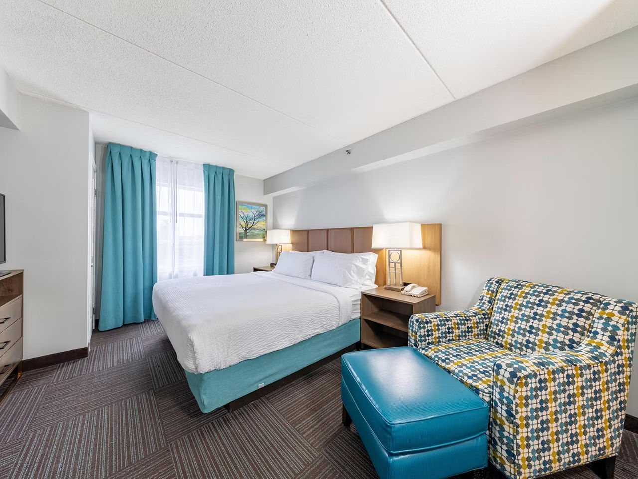 image Wake up in the room with turquoise curtains, a patterned armchair, and a colorful landscape painting on the wall.