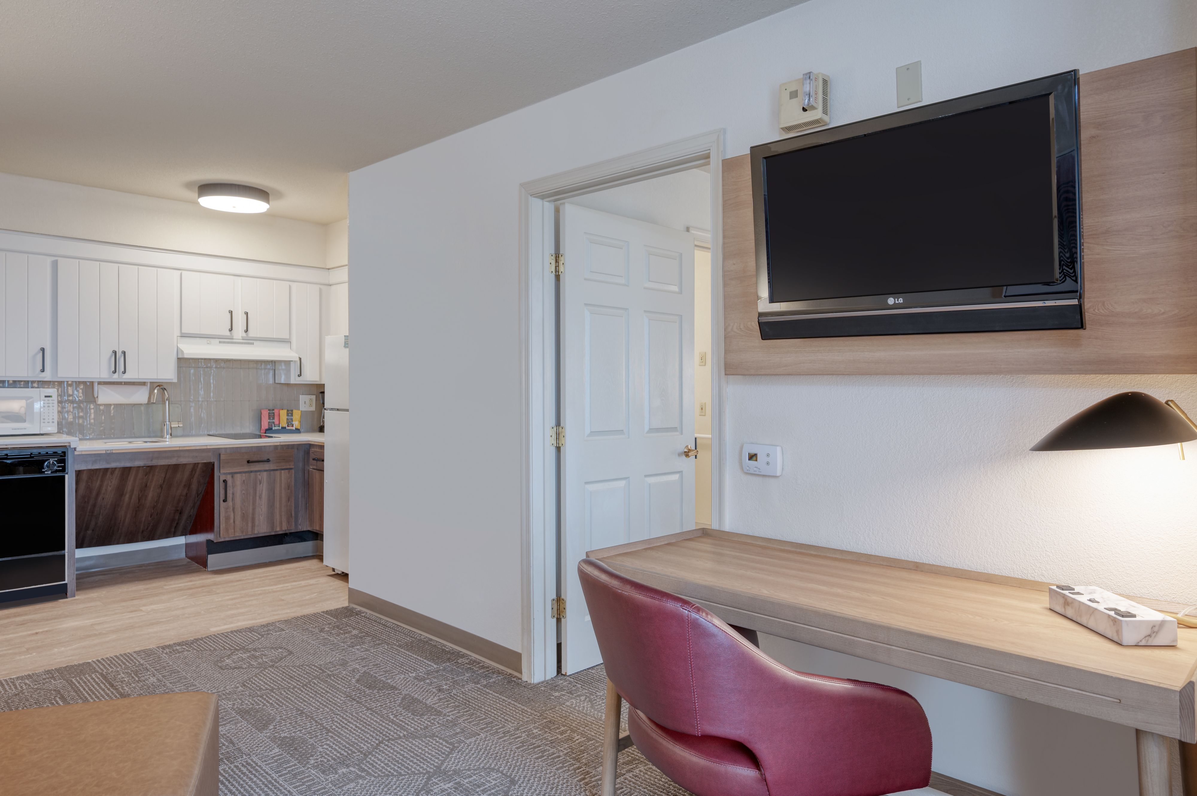 image Living area with kitchen, desk, chair, and wall-mounted TV.