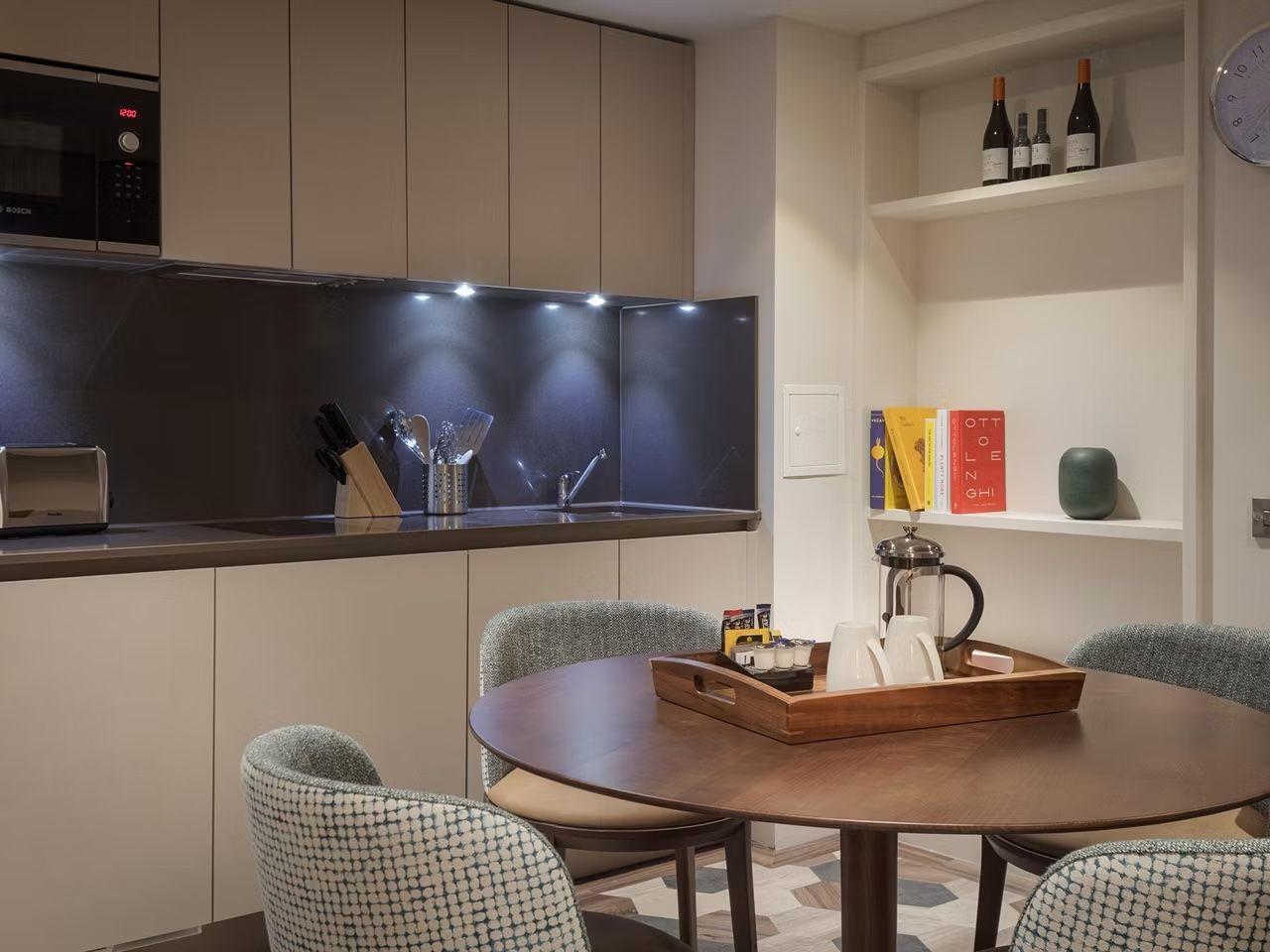 image Kitchen and dining area with round wooden table, teal chairs, microwave, toaster, and French press on the table