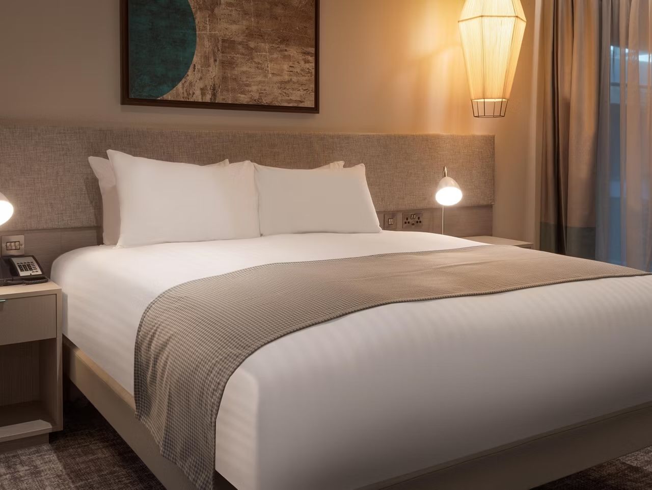 image Bedroom with king bed, beige padded headboard, teal circular artwork, and pendant bedside lamps