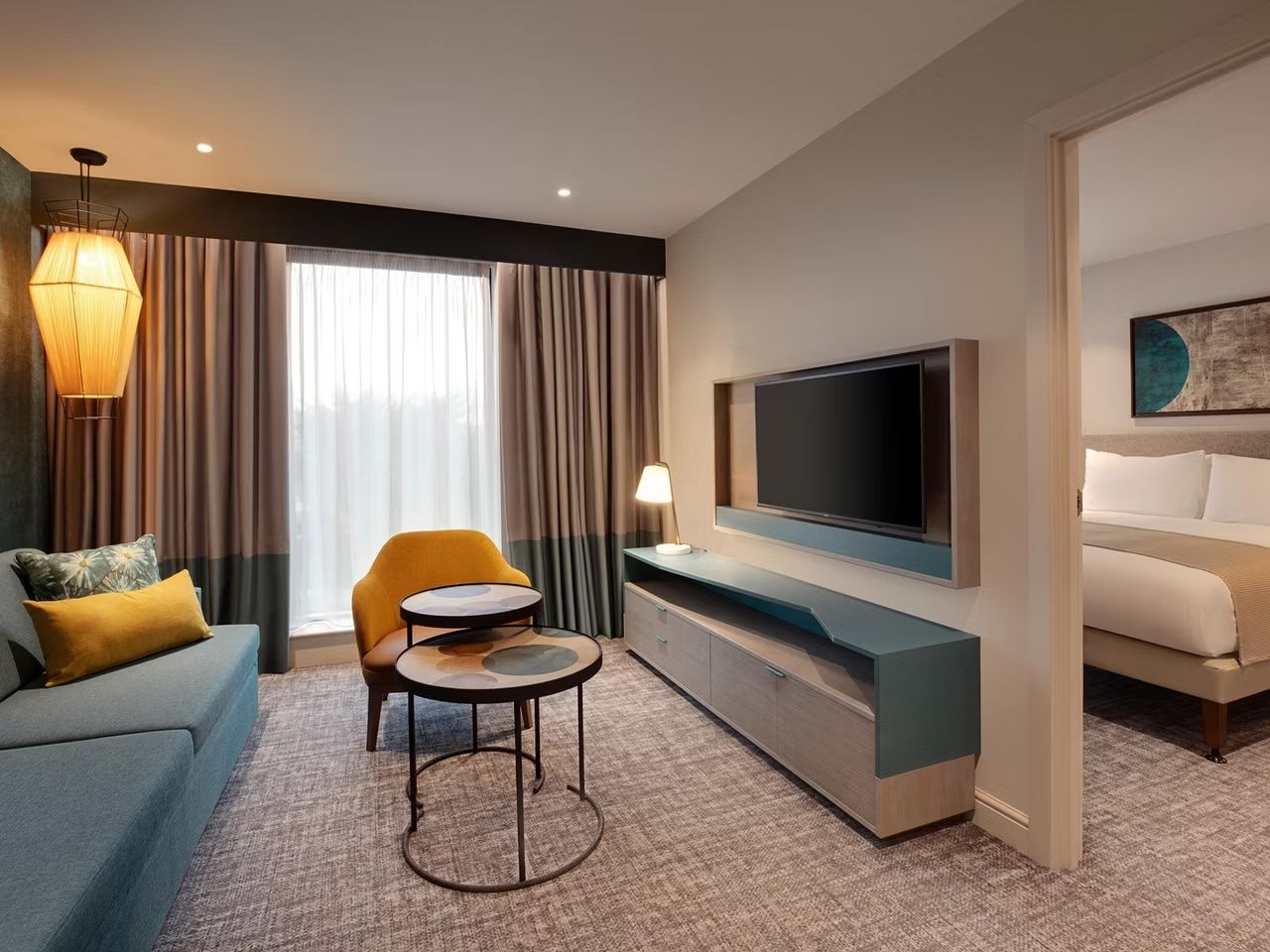 image Living area with teal sofa, orange accent chair, wall-mounted TV, and a view through to the bedroom