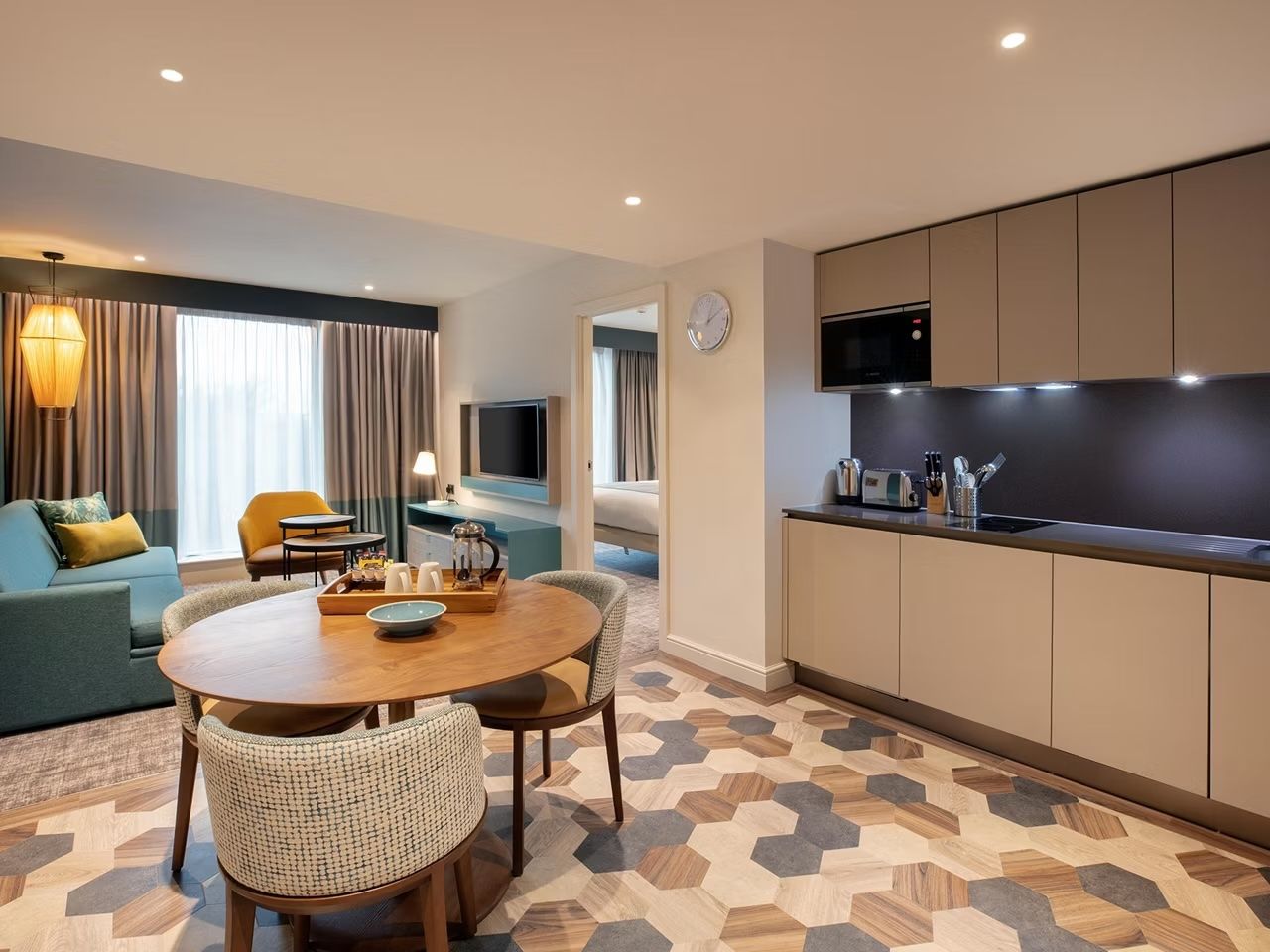 image Open-plan living and kitchen area with blue sofa, round dining table, geometric-patterned floor, and wall-mounted TV
