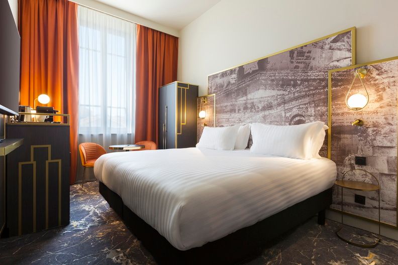 image A classic room with a plush king-size bed, warm stone-effect feature wall, and rich terracotta curtains — elegant comfort in the heart of Nîmes.