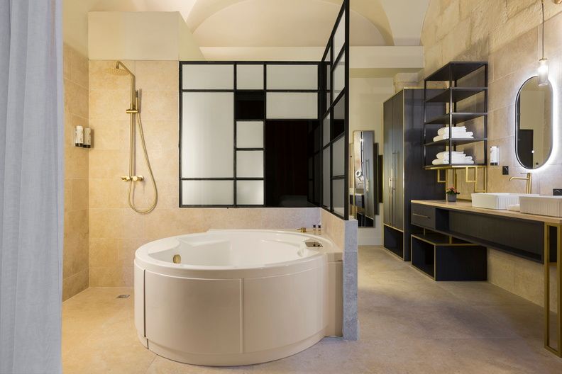 image The deluxe room's luxurious en-suite, with a freestanding corner bathtub, rainfall shower, and sleek black framed glass — a spa-like experience in your own room.