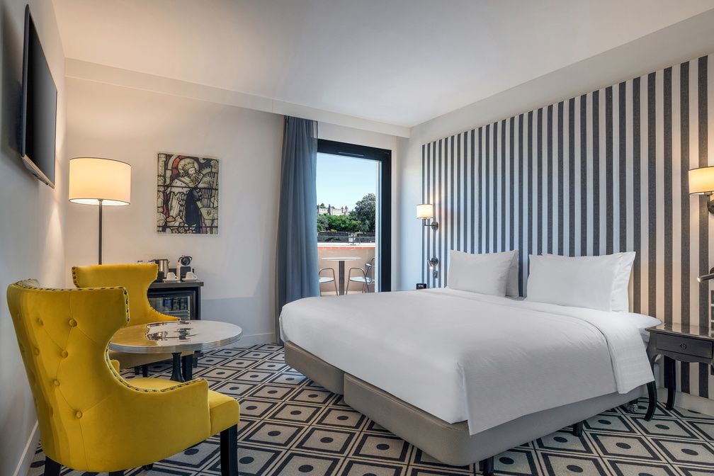 image Striped feature wall, king bed, and a yellow armchair by the window — all rooms are air-conditioned.