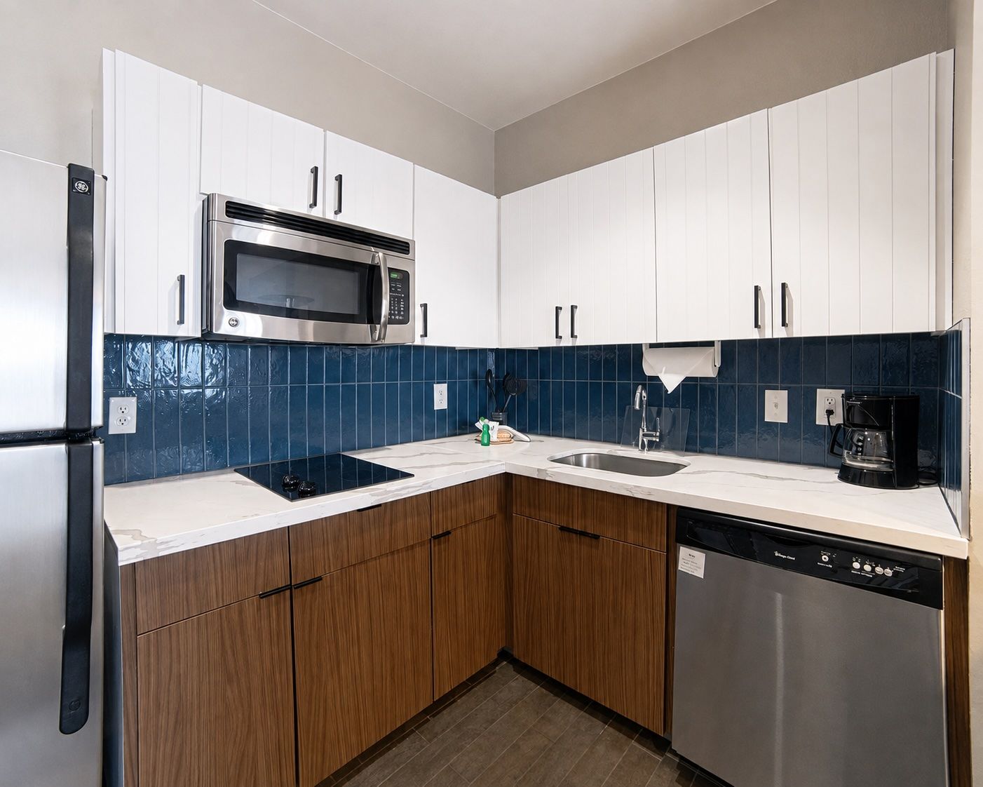 image Compact kitchen with blue tile backsplash, refrigerator, and microwave.