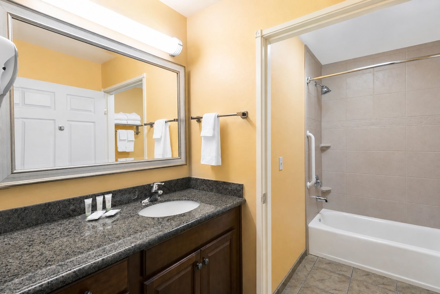 image Accessible bathroom with bathtub, grab bar, and vanity with mirror.