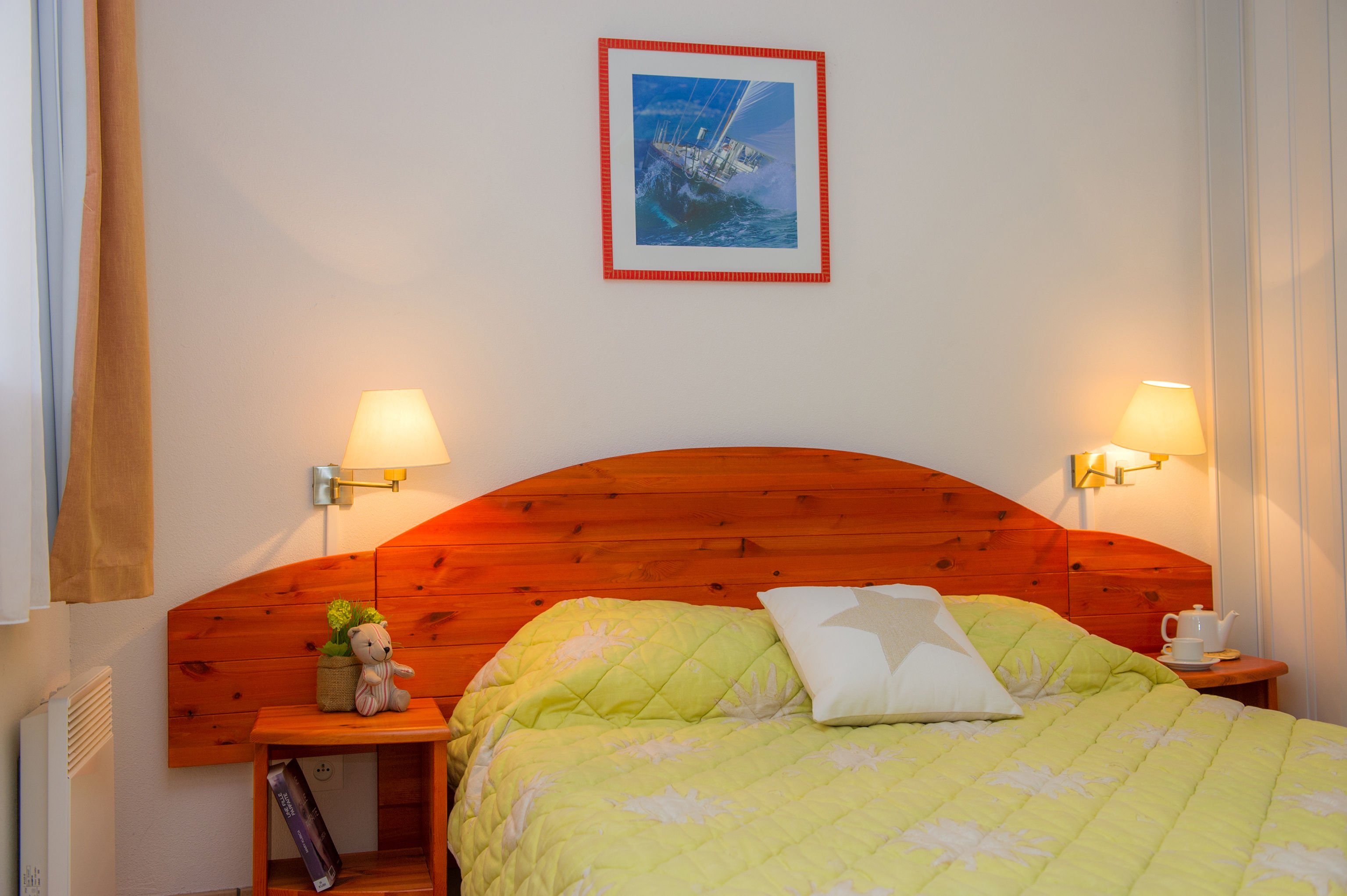 image Double bedroom with light green quilt, wall sconces, and a nautical print above the wooden bed frame.