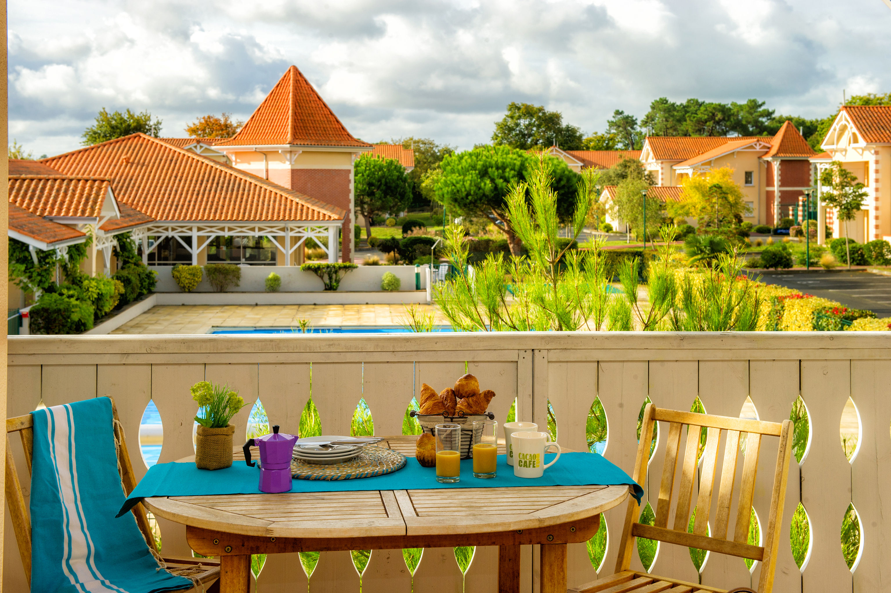 image Furnished terrace with pool and red-roofed building views — breakfast with croissants included in the scene.
