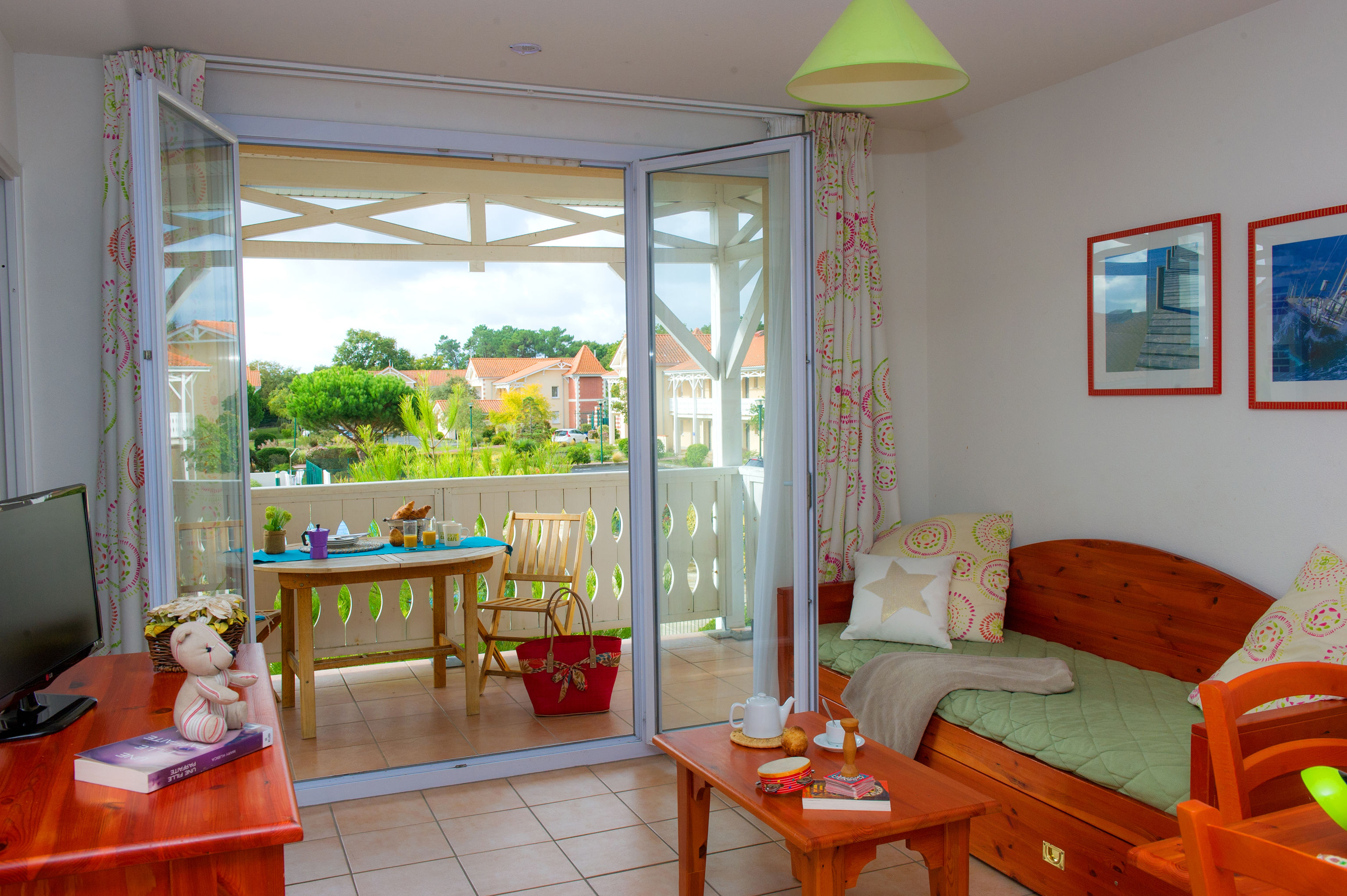 image Living area with wooden daybed, green bedding, TV, and doors opening to the terrace.