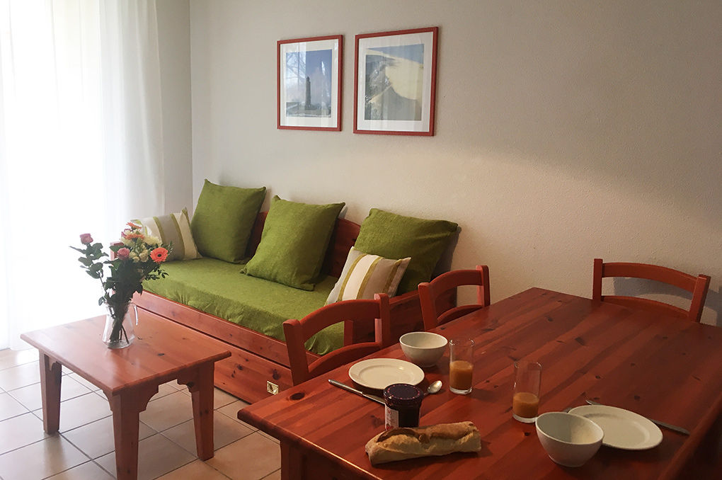 image Dining space with wooden table and chairs, daybed with green cushions, and light-filled sheer curtains.