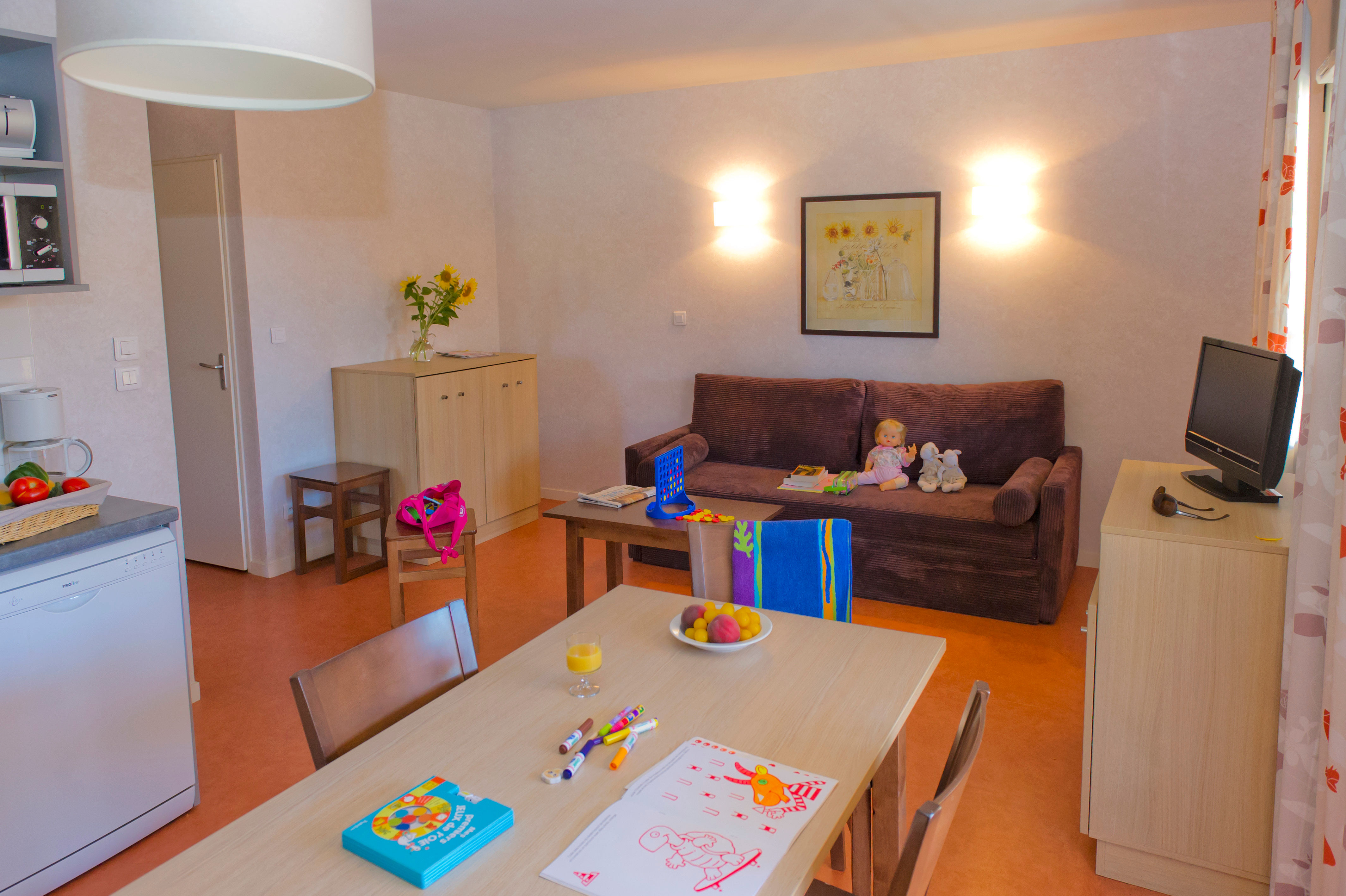 image Living area with a brown sofa bed, TV unit, and dining table — the kitchen sits just off to the left.