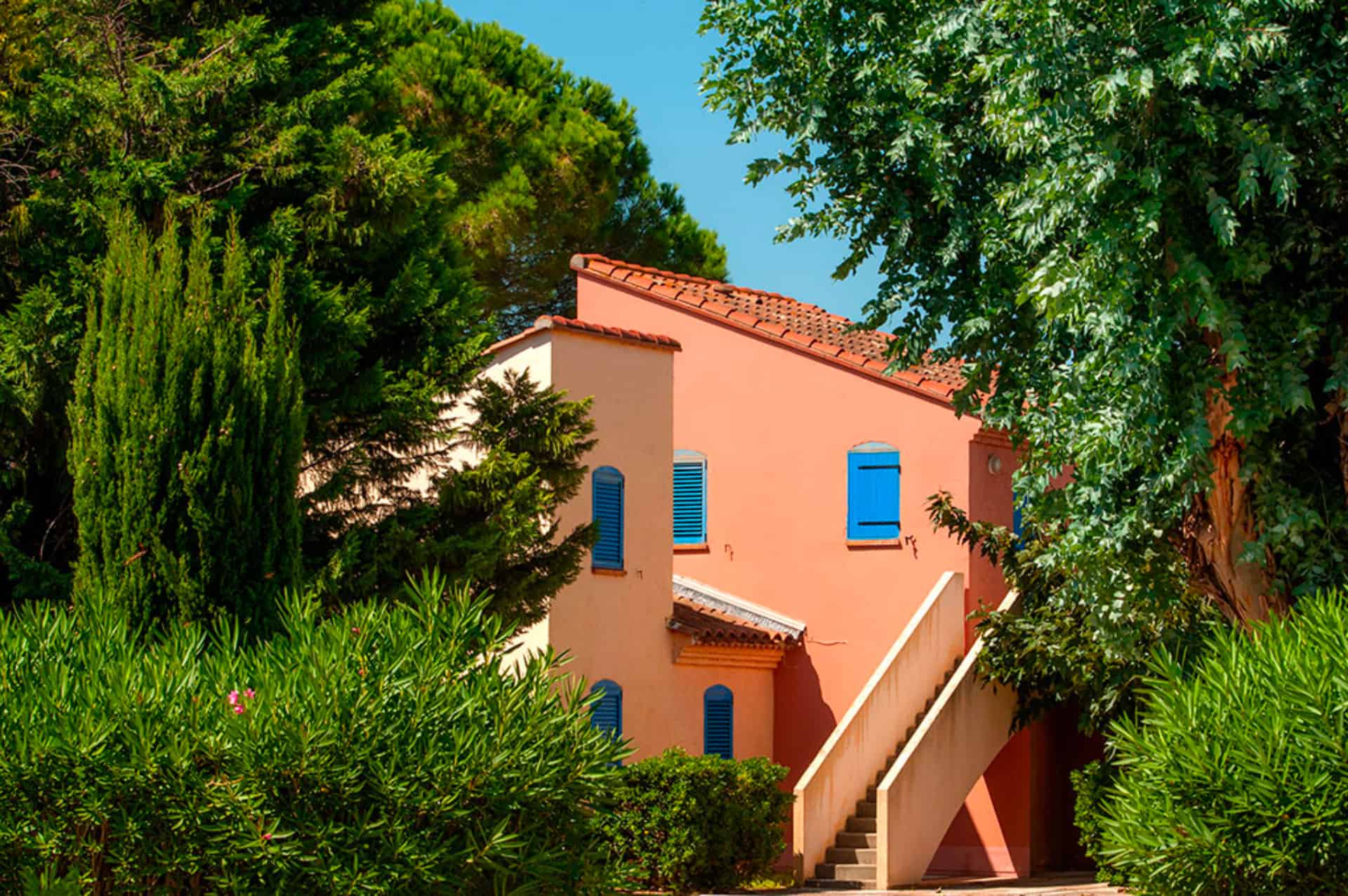 image The terracotta-roofed Hameau building with blue shutters, set among the domain's mature gardens.