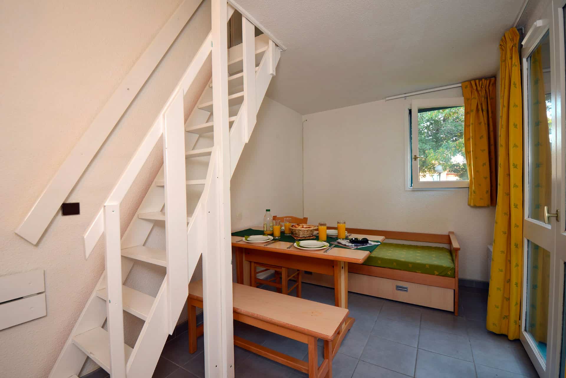 image A cosy dining corner with bench seating and yellow curtains, ideal for family breakfasts before the beach.