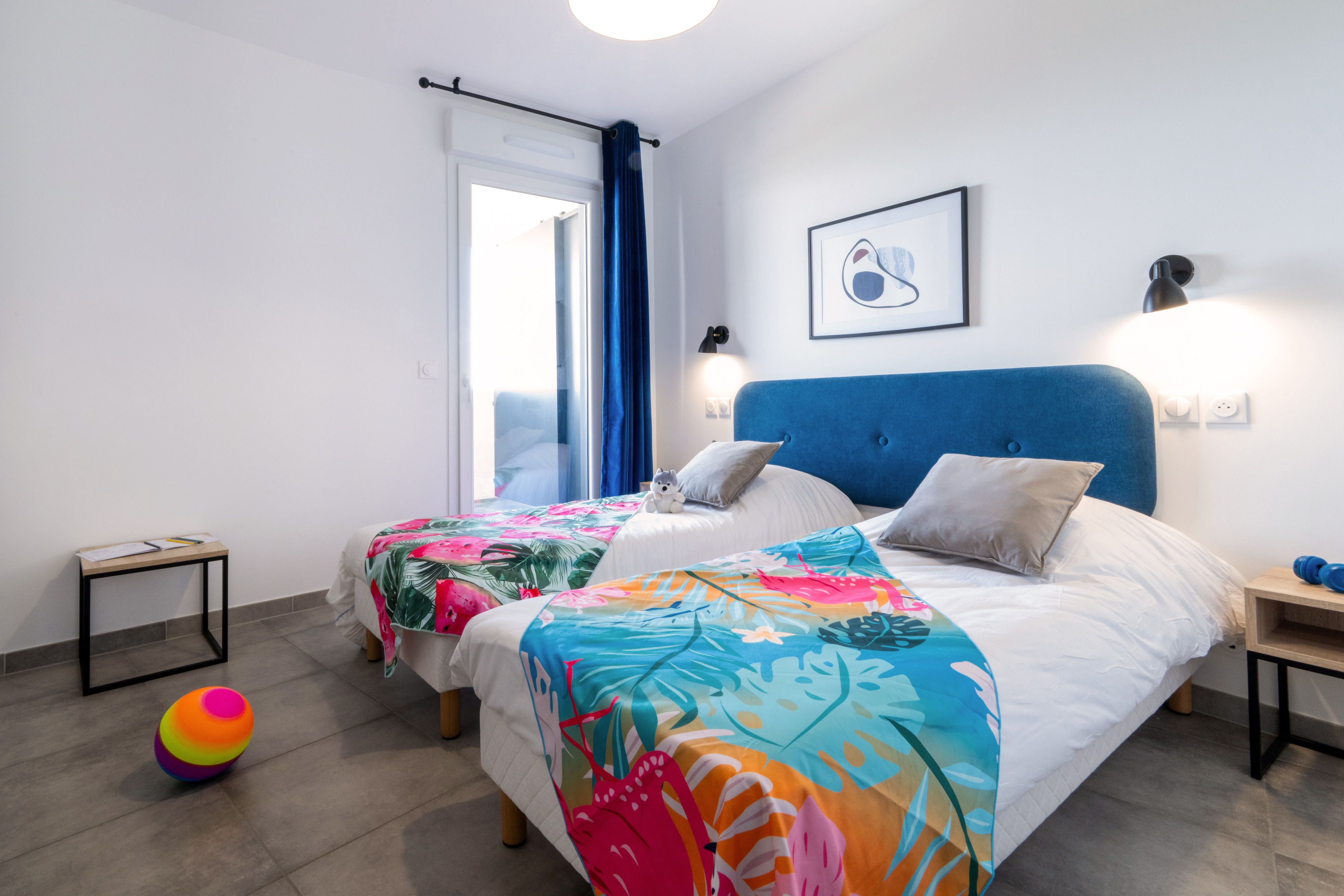 image Second bedroom with two single beds, tropical-patterned spreads, and blue curtains — a bright, independent room for the rest of the group.