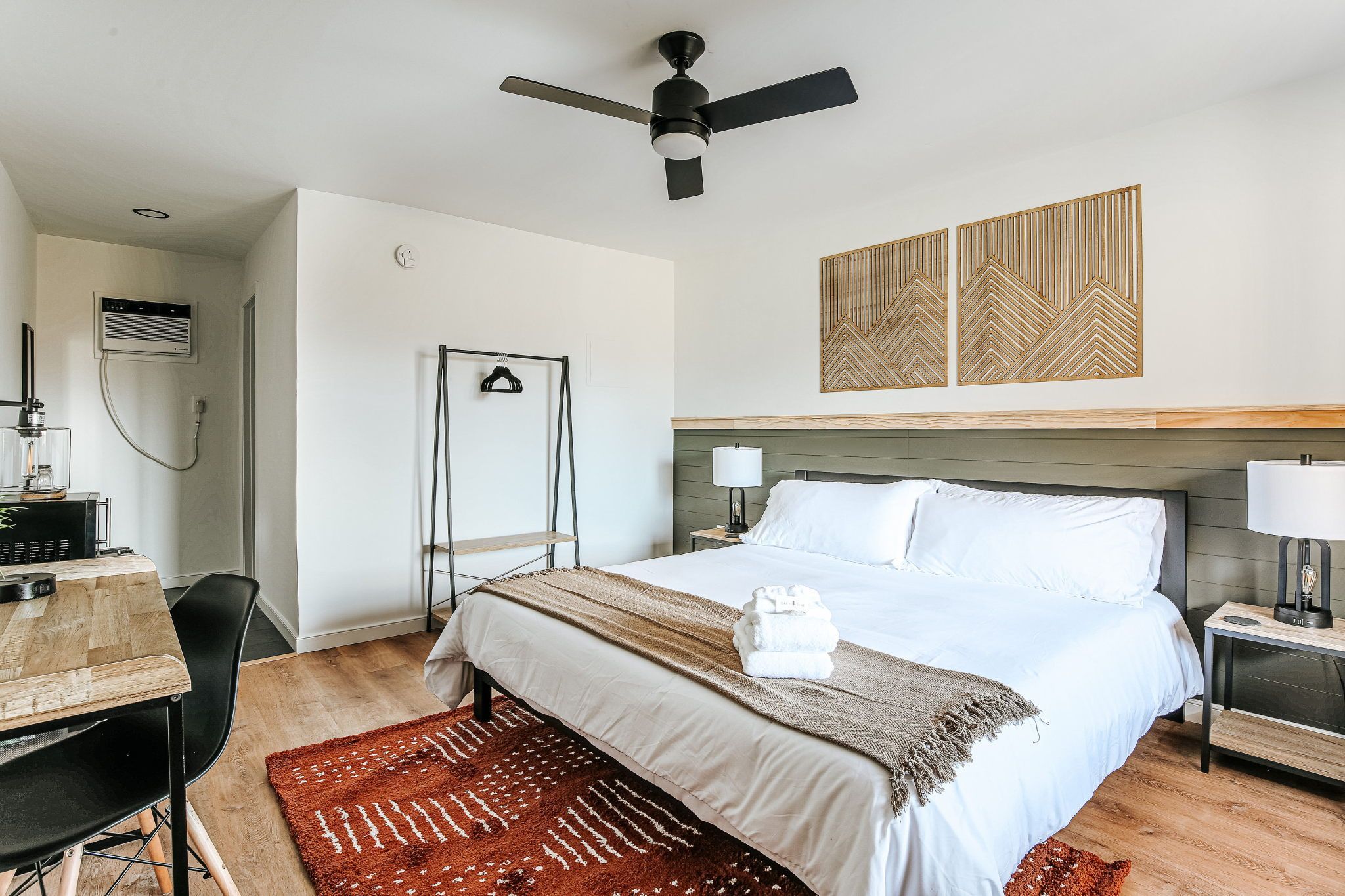 image A serene space awaits with wood accents, a comfortable workspace, and a delightful pop of color from the area rug.