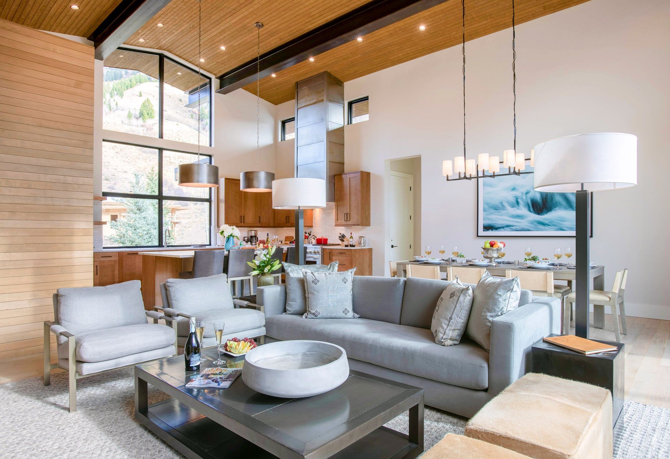 image Open living area with a grey sectional sofa, wood-paneled walls, and a dining table and kitchen visible beyond