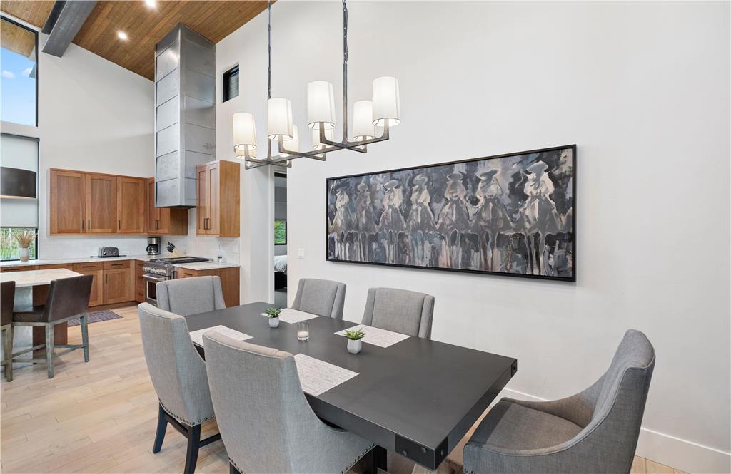 image Dining table beneath a modern chandelier, with grey upholstered chairs and abstract art on the wall