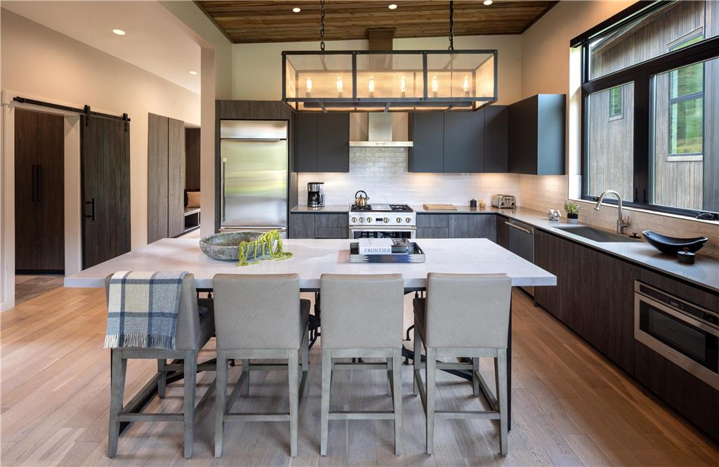 image Kitchen with dark cabinetry, a sliding barn door, and a six-seat island beneath wood-beam ceilings