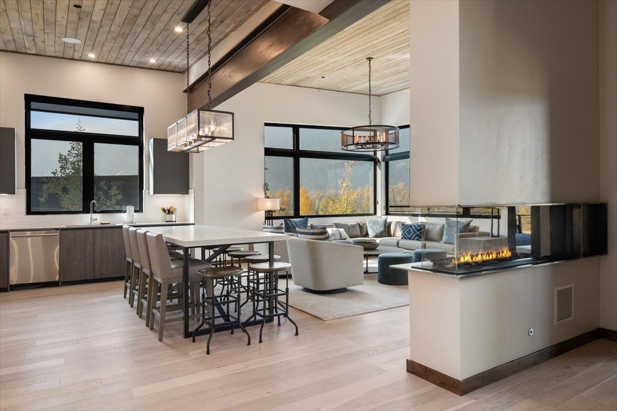 image Open kitchen and living area with a six-seat island, linear fireplace, and mountain views through the glass wall