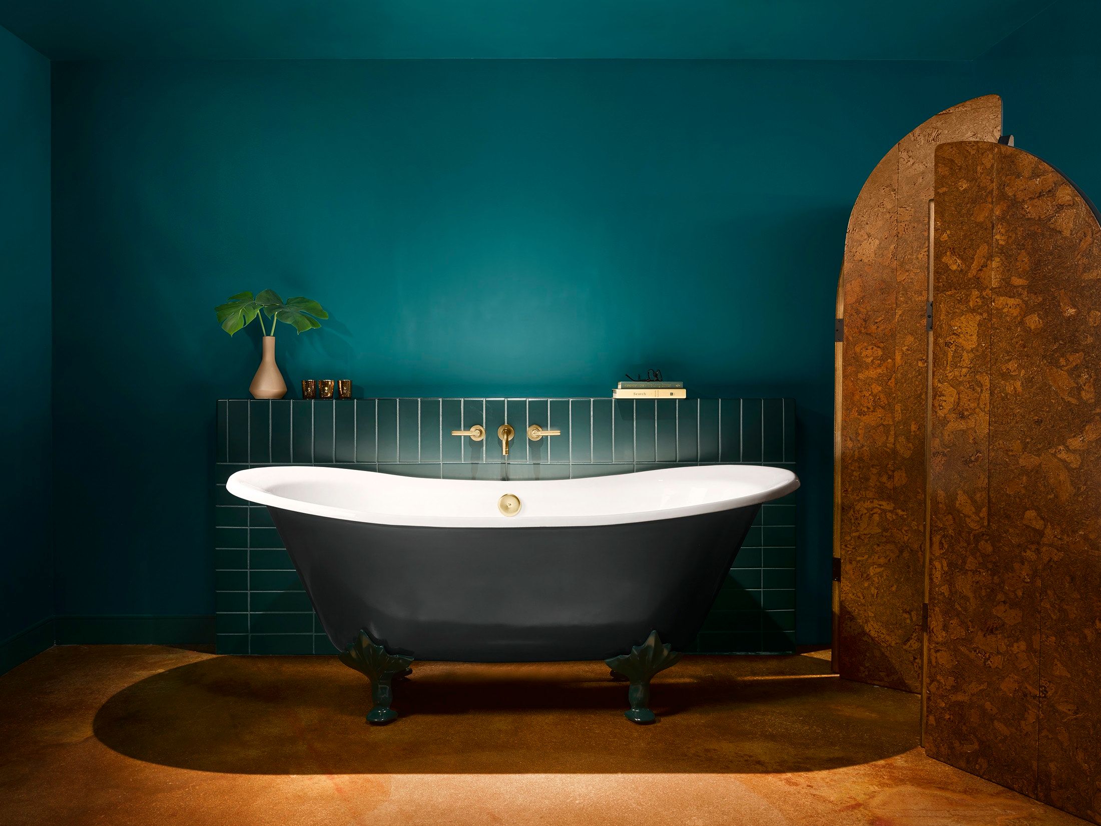 image Dark grey freestanding tub with ornate metal feet against a deep teal wall, with glossy green tiles and trailing foliage