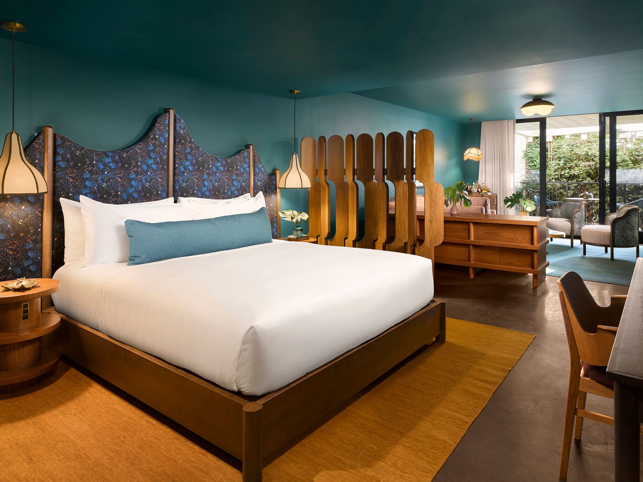 image King bed with a patterned dark blue headboard against a teal wall, with wooden nightstands and warm-toned rugs on the floor