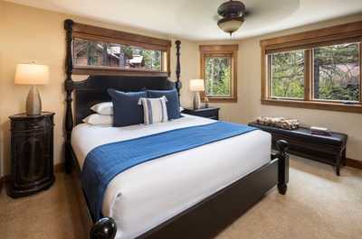 A king bed sits under a ceiling fan, with windows facing the trees.