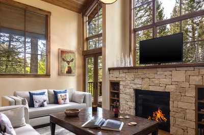 Floor-to-ceiling windows fill the living area with light, framing the stone fireplace at its center.
