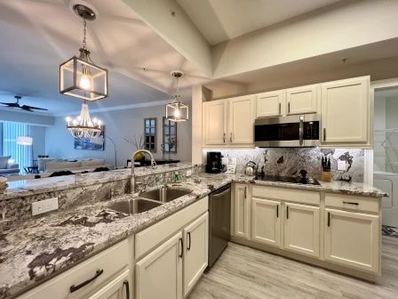 image Kitchen with beige cabinets, granite countertops, pendant lights, and stainless appliances