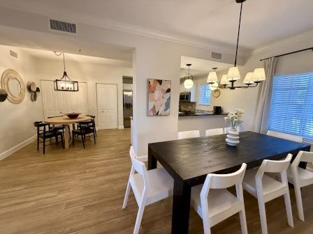 image Dining area with a black table, white chairs, wood flooring, and a hanging light fixture