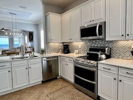 image Kitchen with white cabinets, marble countertops, silver appliances, and a tile backsplash