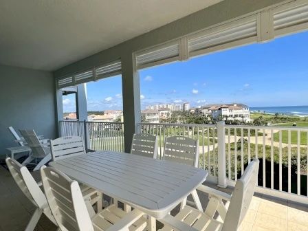 image Balcony dining area with white outdoor furniture and views of the lawn and ocean beyond