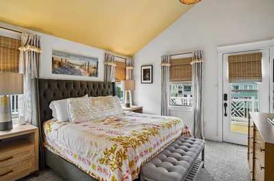 Bedroom with a floral comforter, sunlit windows, and cheerful nautical art.