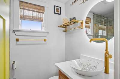 Compact bathroom adorned with gold accents and a stylish round vessel sink.