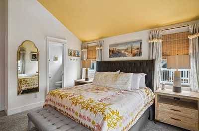 Bright bedroom with a large bed beneath a golden yellow ceiling and framed art.