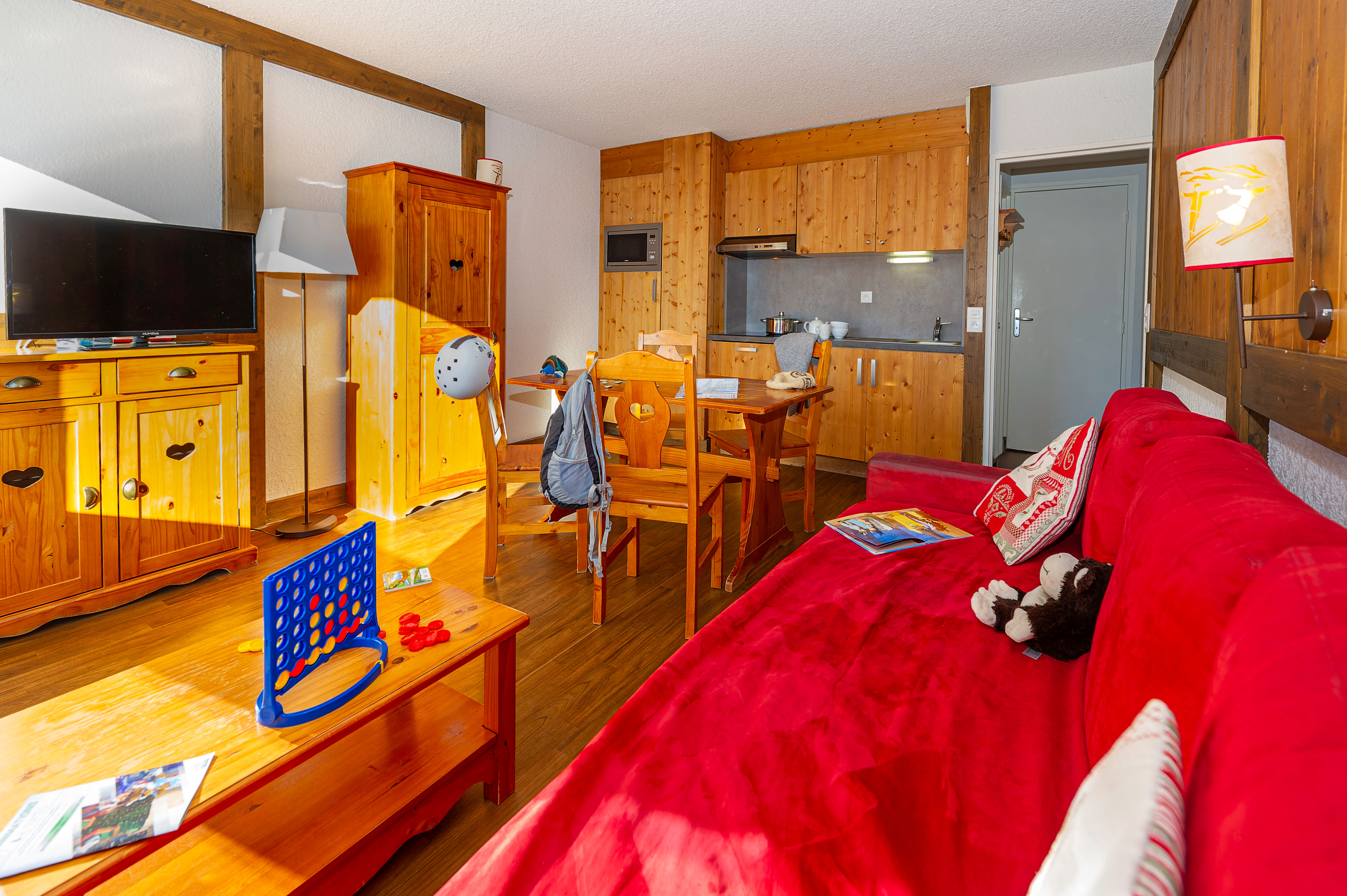 image Living area with a red sofa, wooden furniture and the kitchenette beyond