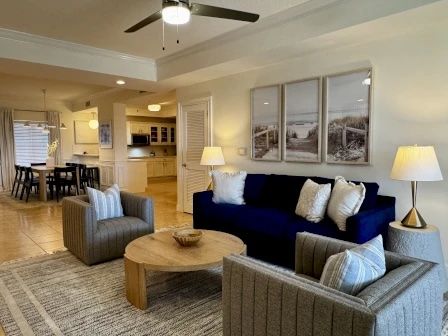 image Living area with navy blue sofa, ceiling fan overhead, and natural light from the balcony windows