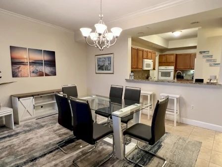 image Glass dining table beneath a modern chandelier — open to the kitchen and balcony