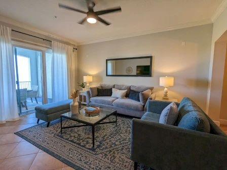 image Living area with plush grey sectional, sheer curtains, and a sliding door to the private balcony
