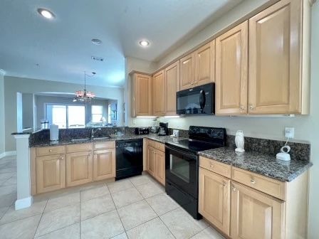 image Kitchen with warm wood cabinetry, black appliances, and full counter space for group cooking