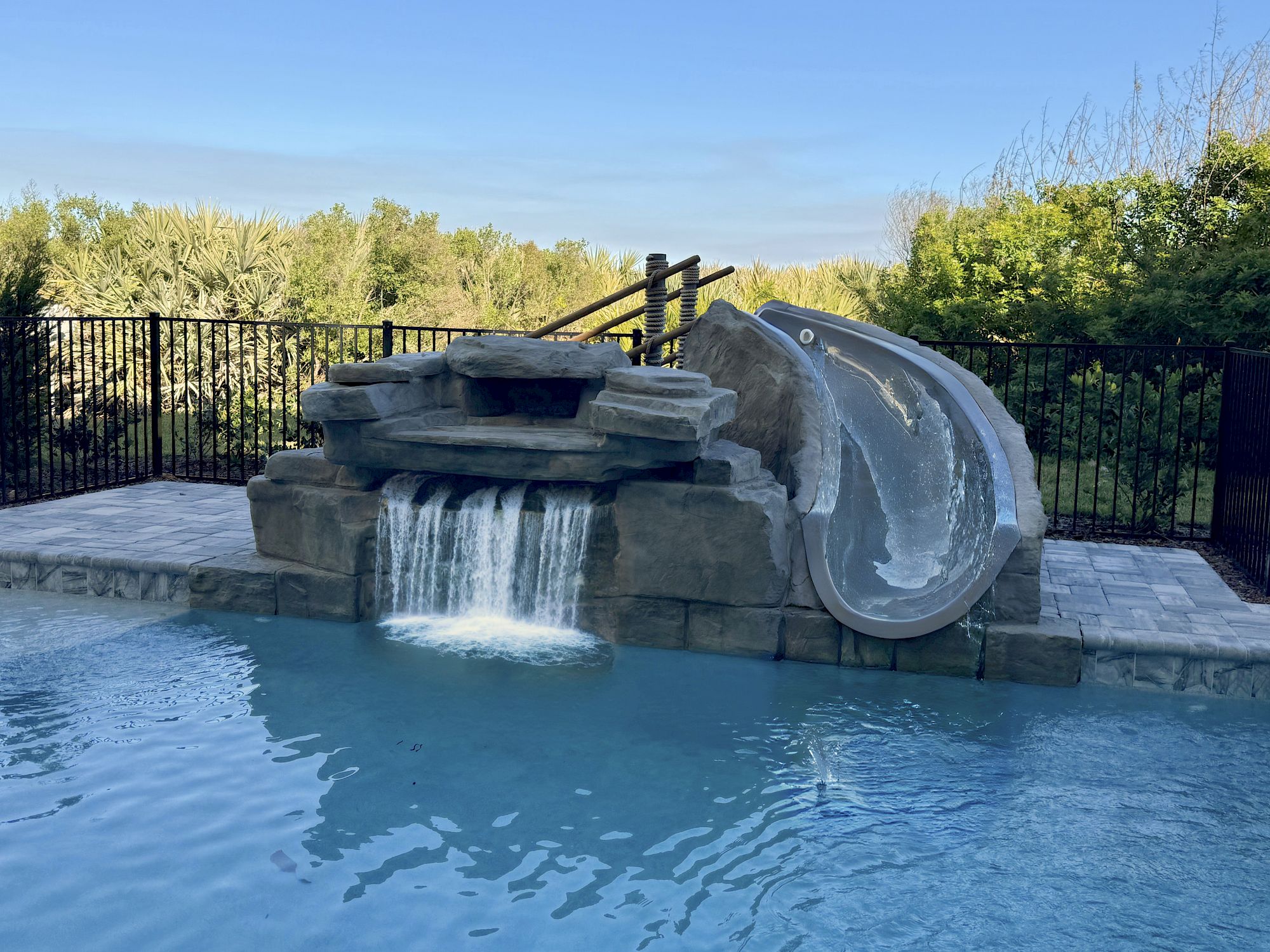 image Private pool with waterfall feature and clear blue water — multiple balconies overlook from above