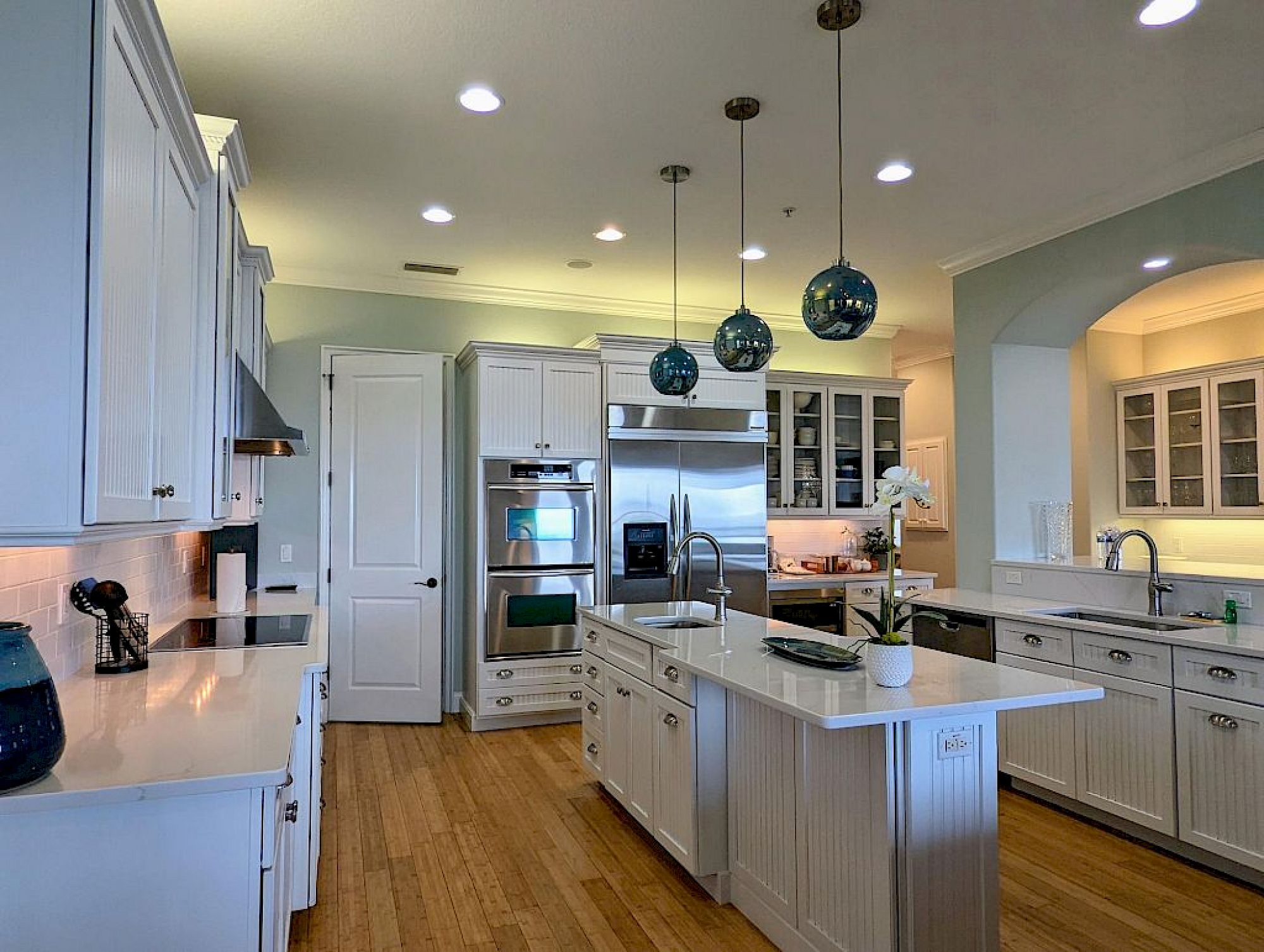 image Kitchen with white beadboard cabinetry, white quartz counters, blue pendant lights, and island sink