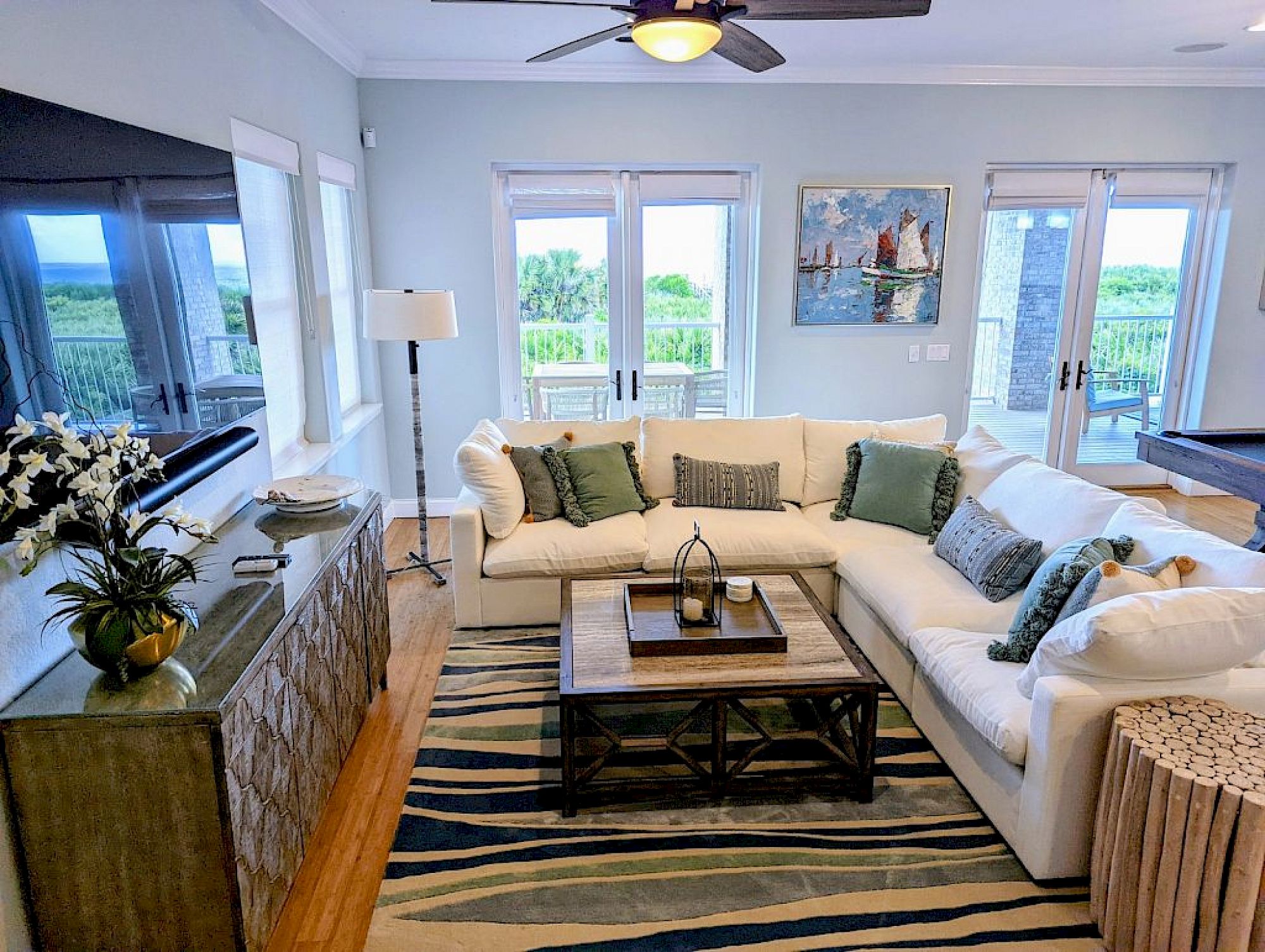 image Living room with light grey L-shaped sofa, log-style side table, and large windows with outdoor views