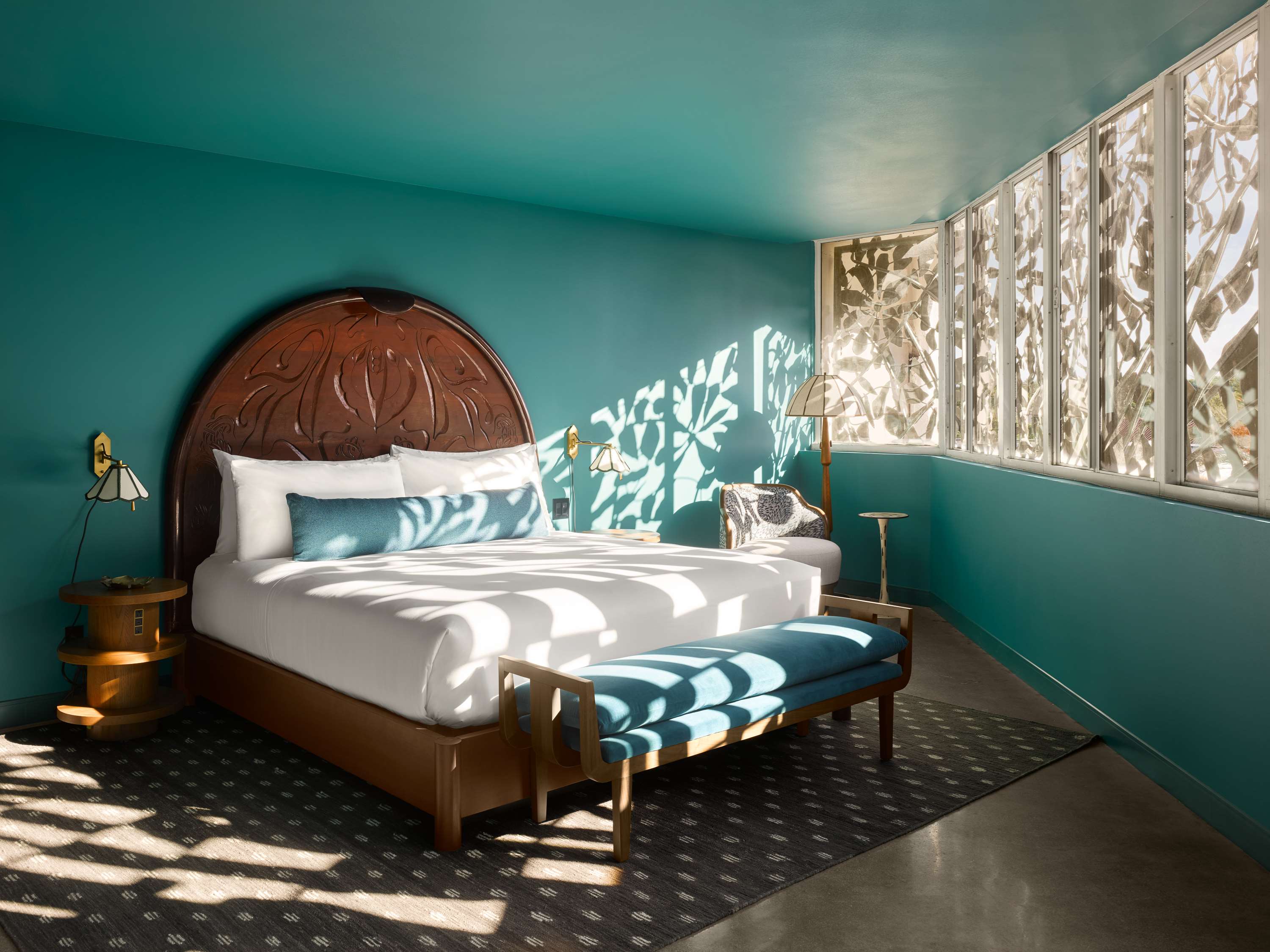 image King bedroom with a hand-carved mahogany arch headboard, teal walls, brass sconces, and wraparound corner windows