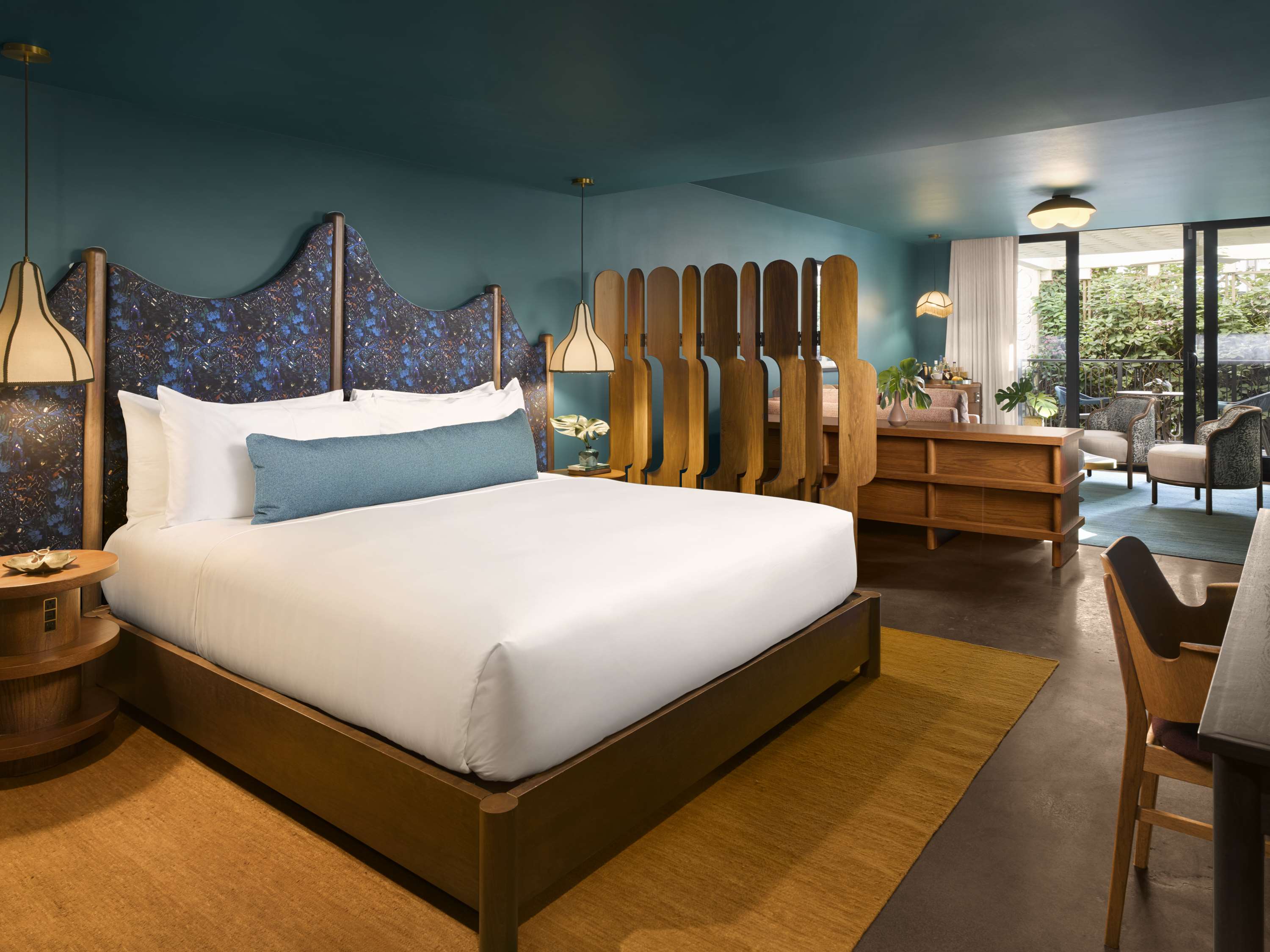 image King bed with an iridescent floral headboard, teal walls, and a walnut room divider separating the sleeping and living areas