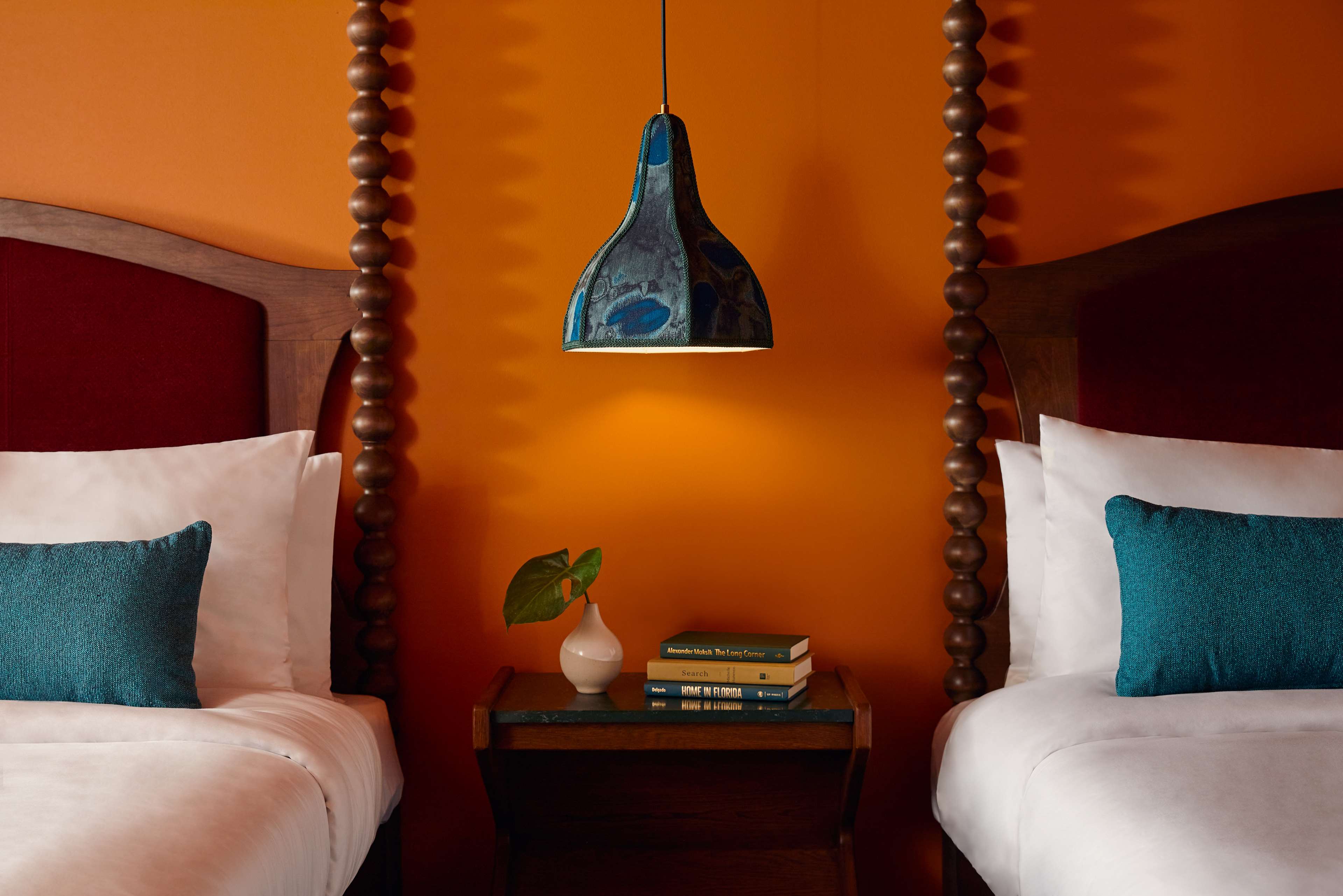 image Between two spool-post beds, a dark wood nightstand with stacked books and an iridescent blue pendant lamp overhead