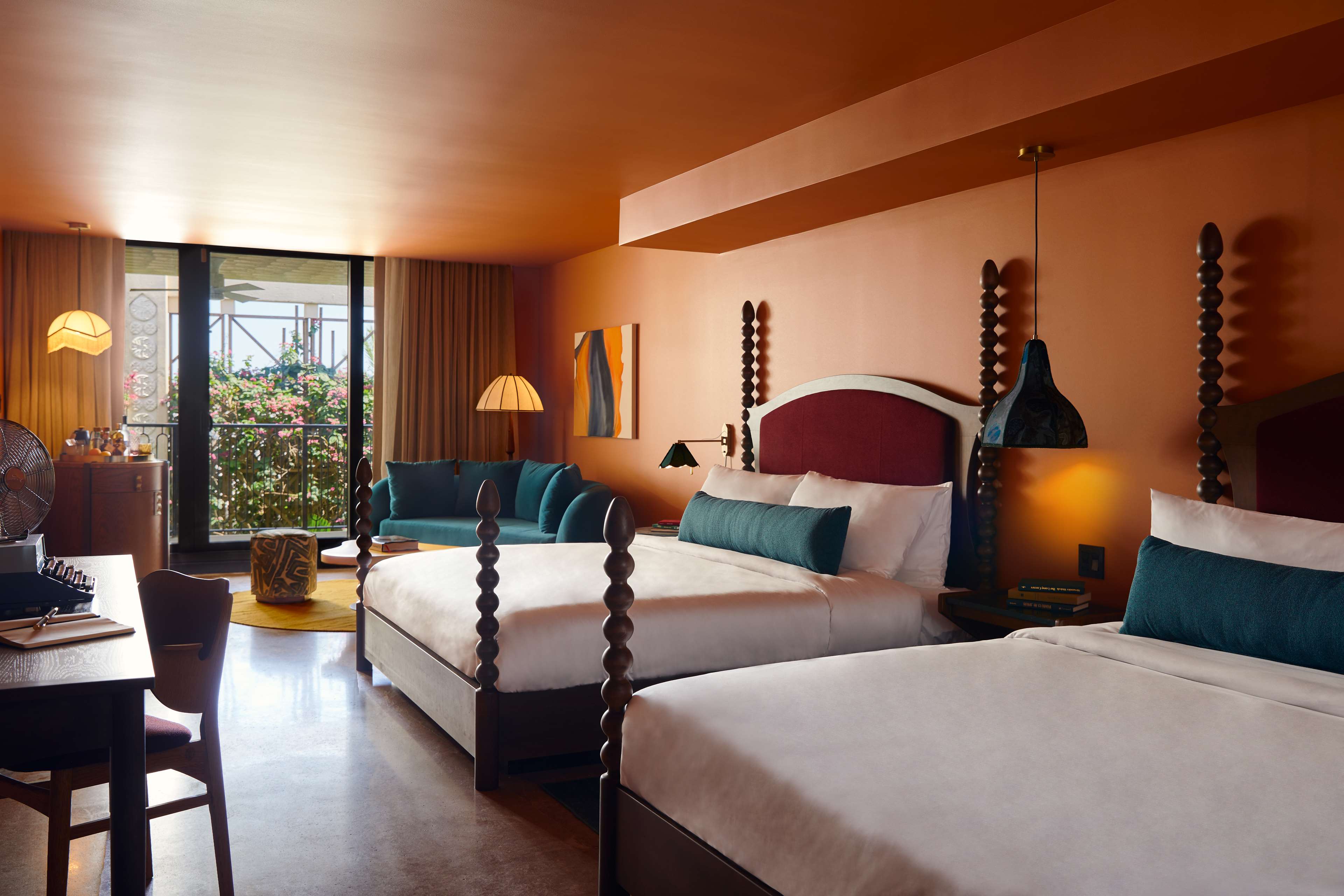 image Wide view of both king beds, teal sofa, and the balcony beyond — the full room layout in warm terracotta tones