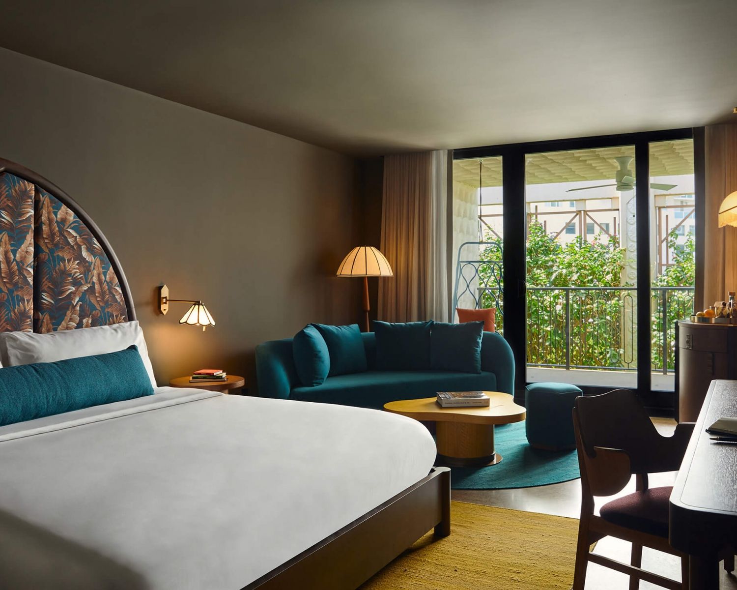 image King bed with a botanical-print arch headboard, teal velvet sofa, and floor-to-ceiling balcony door overlooking the garden