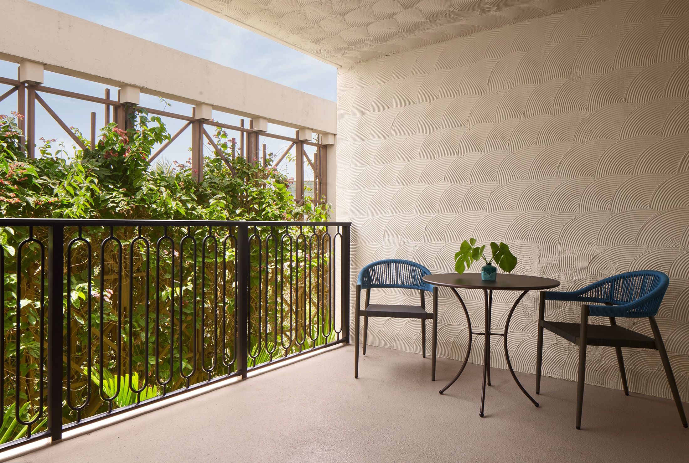 image Private balcony with two blue rope chairs, a round bistro table, and a textured white wall — a garden-facing retreat