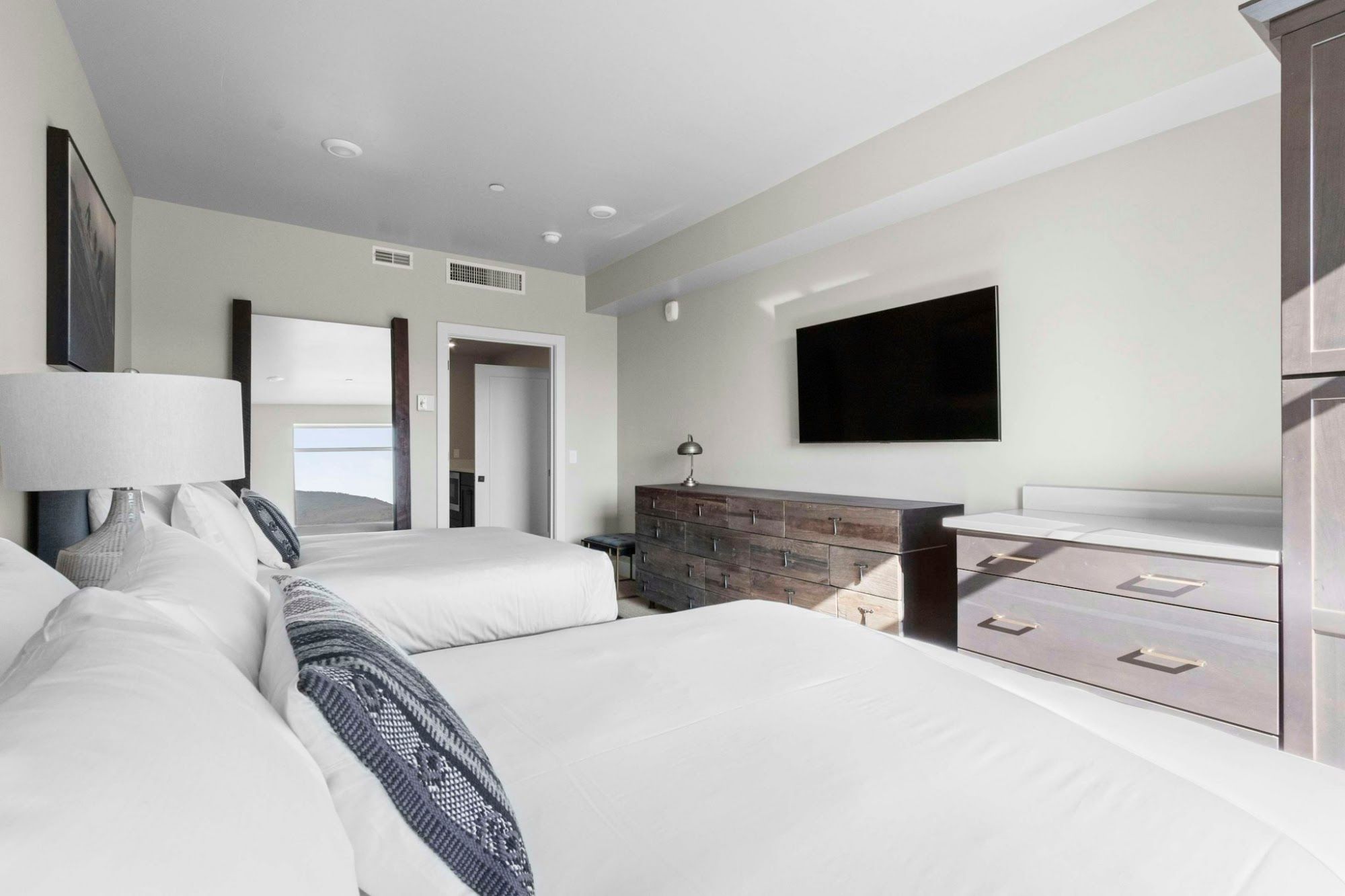 image Two queen beds with white bedding, wall-mounted TV, and storage dresser